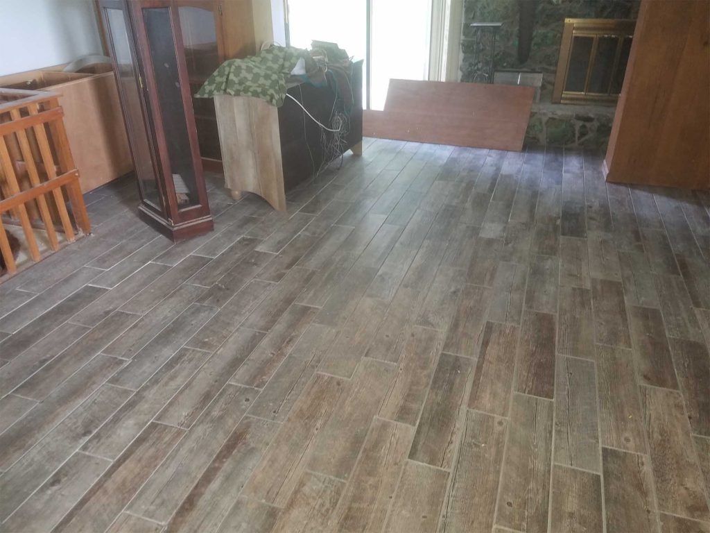 Wood-look tiled room with wooden furniture, a potted plant, and a rug near the back doorway.
