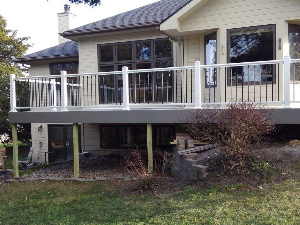 House with raised deck, white railing, and stairs overlooking a grassy yard