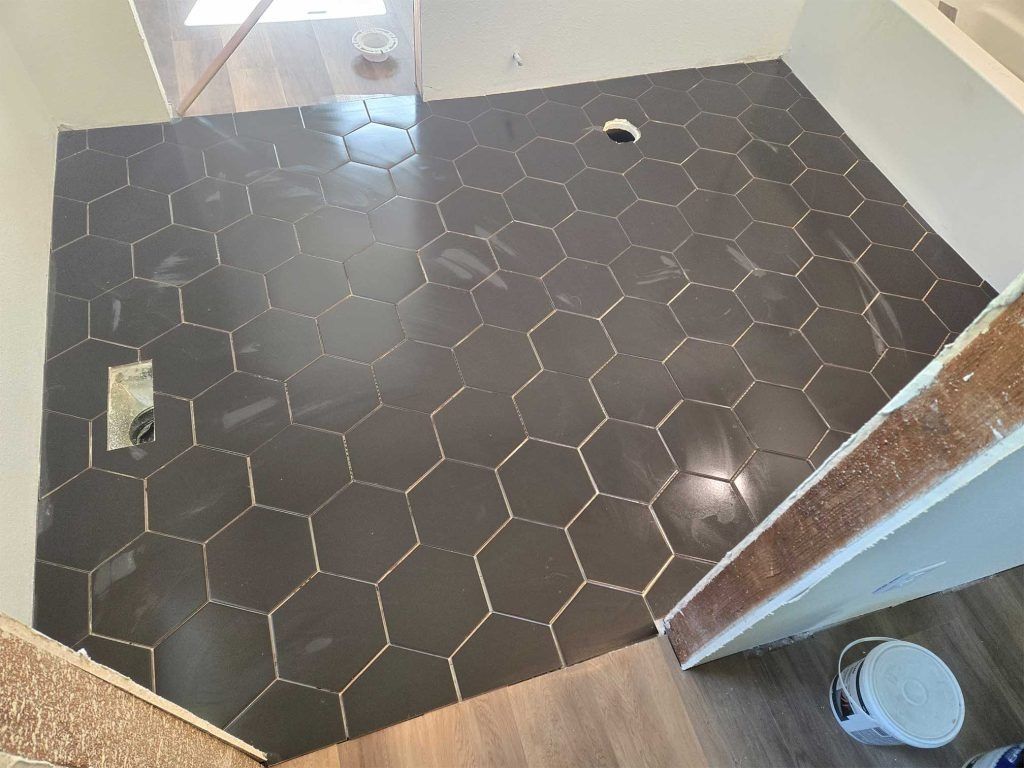 Small bathroom with black hexagon tile floor, shower drain, and toilet visible through the doorway.