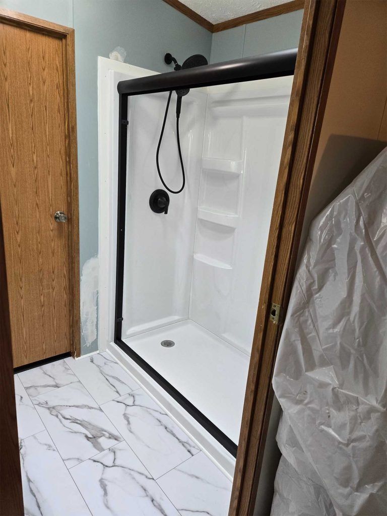 Modern shower stall with black frame, white walls, and marble-pattern tile floor in a bathroom