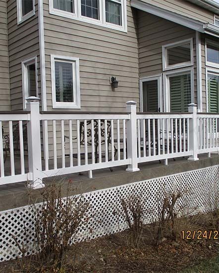 House exterior with beige siding, white porch railings, and lattice skirting in a yard.