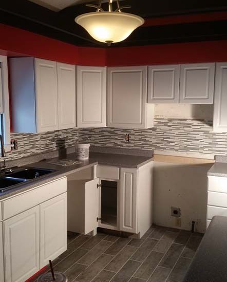 Modern kitchen with white cabinets, gray tile floor, and dark countertops under a red ceiling.
