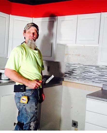 Worker installing kitchen cabinets in a room with white cabinets, red ceiling, and tiled backsplash