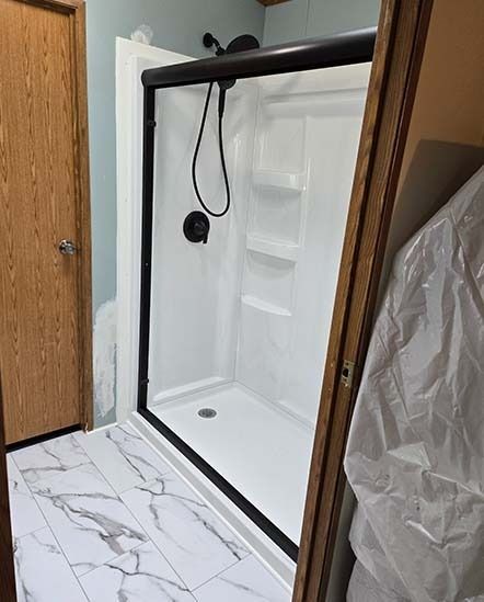 White shower stall with black trim and rainfall showerhead inside a bathroom.