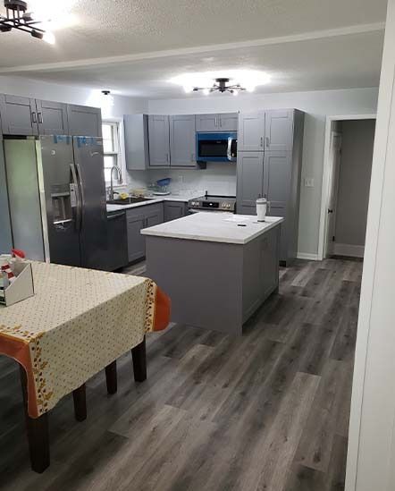 Modern kitchen with gray cabinets, stainless fridge, central island, and wood-look flooring