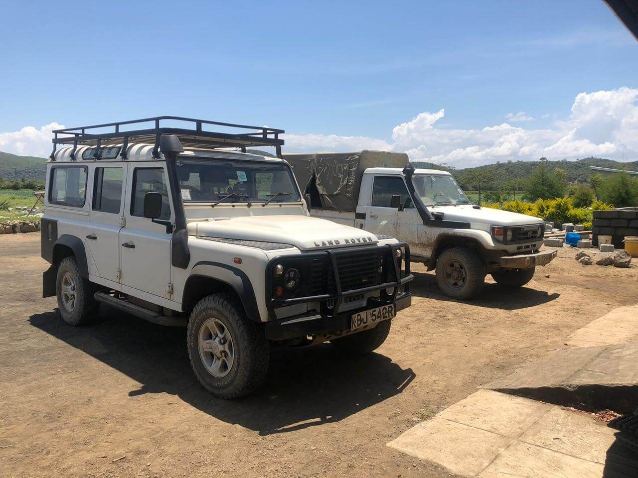 A white jeep and a white truck are parked next to each other on a dirt road.