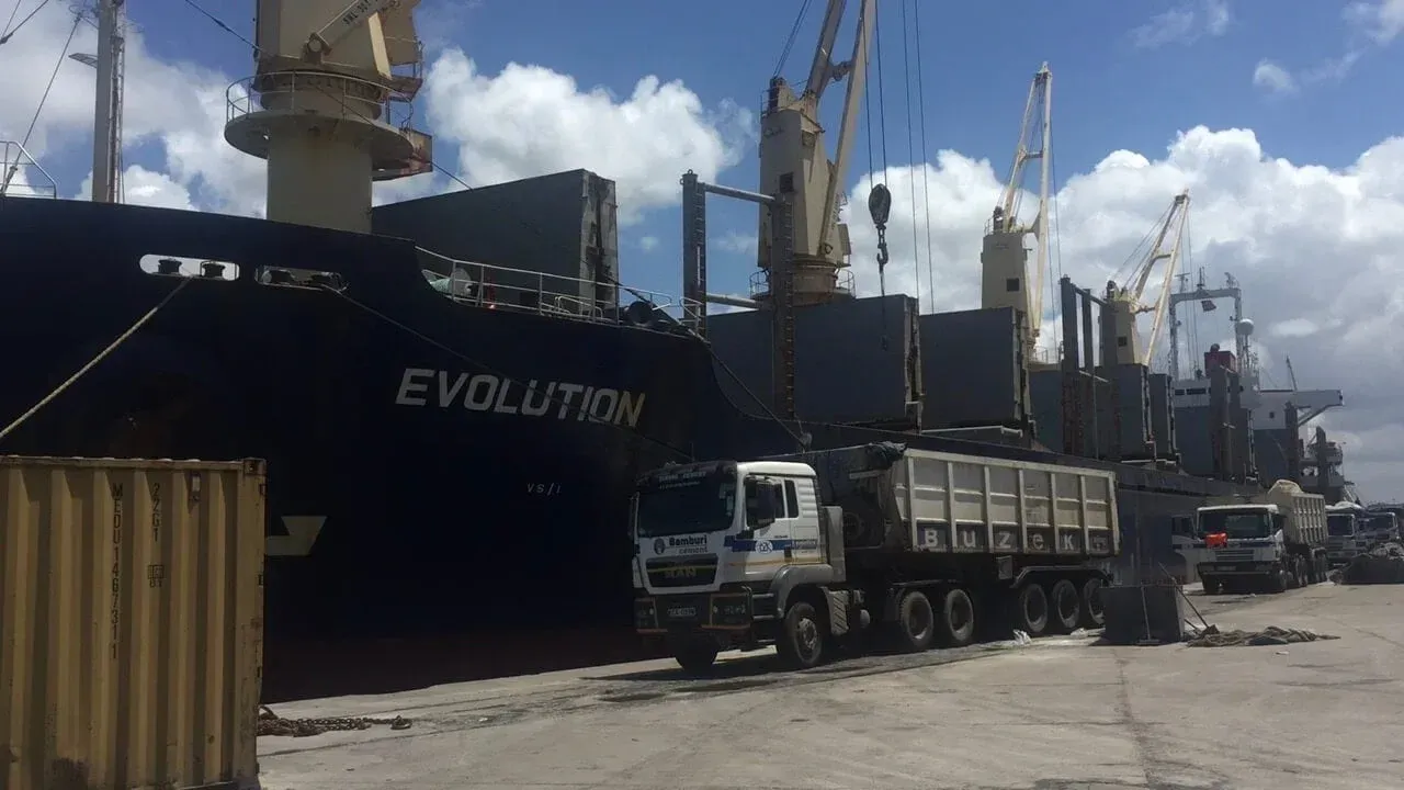 A truck is parked in front of a large ship.