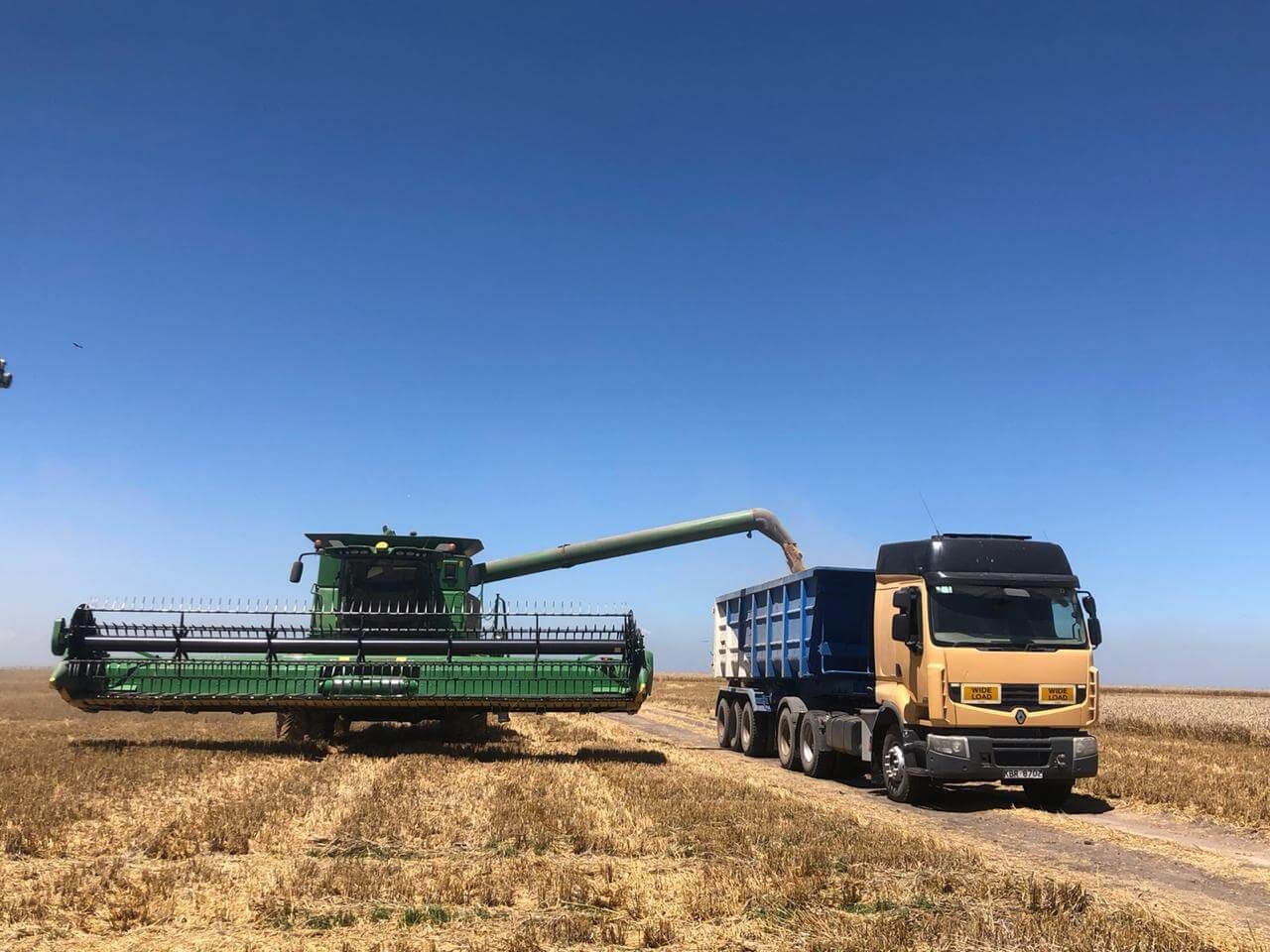 A combine harvester is being loaded into a dump truck in a field.