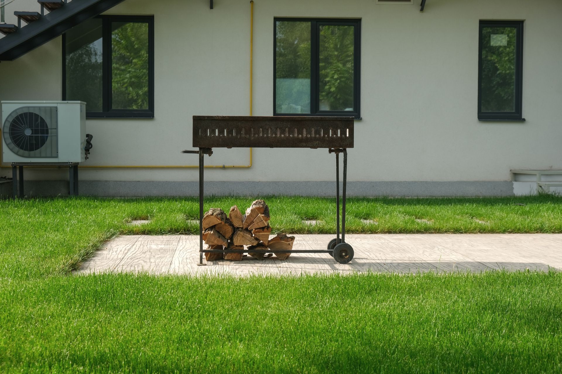 A barbecue grill is sitting in the grass in front of a house.
