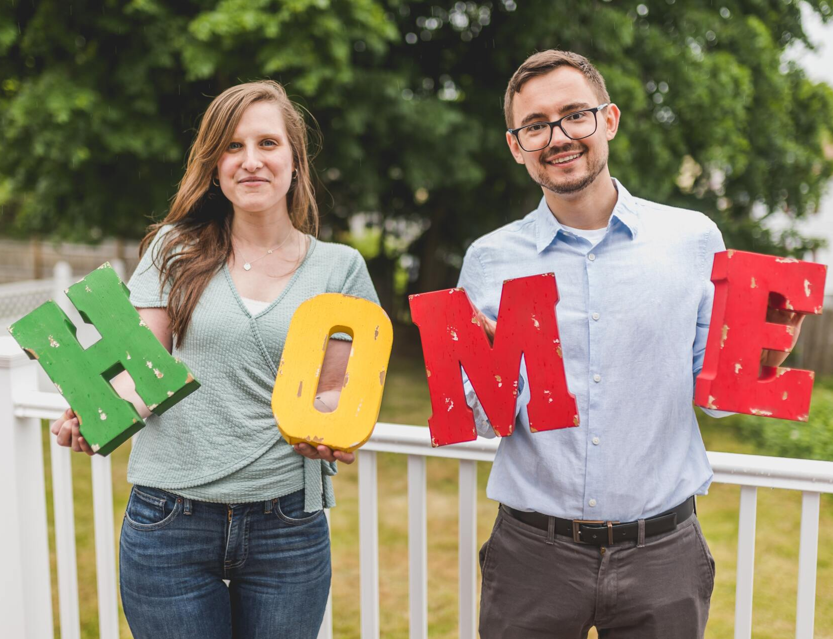 A couple stands on a porch holding large, colorful letters that spell