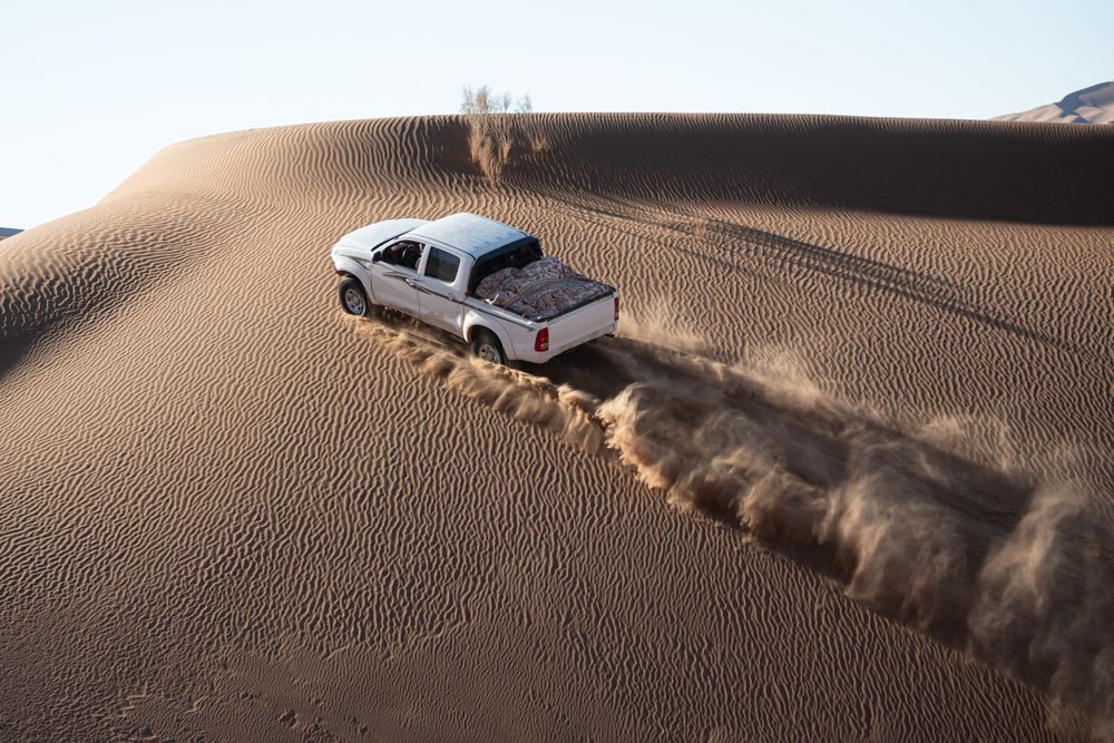A white truck is driving down a sand dune in the desert.