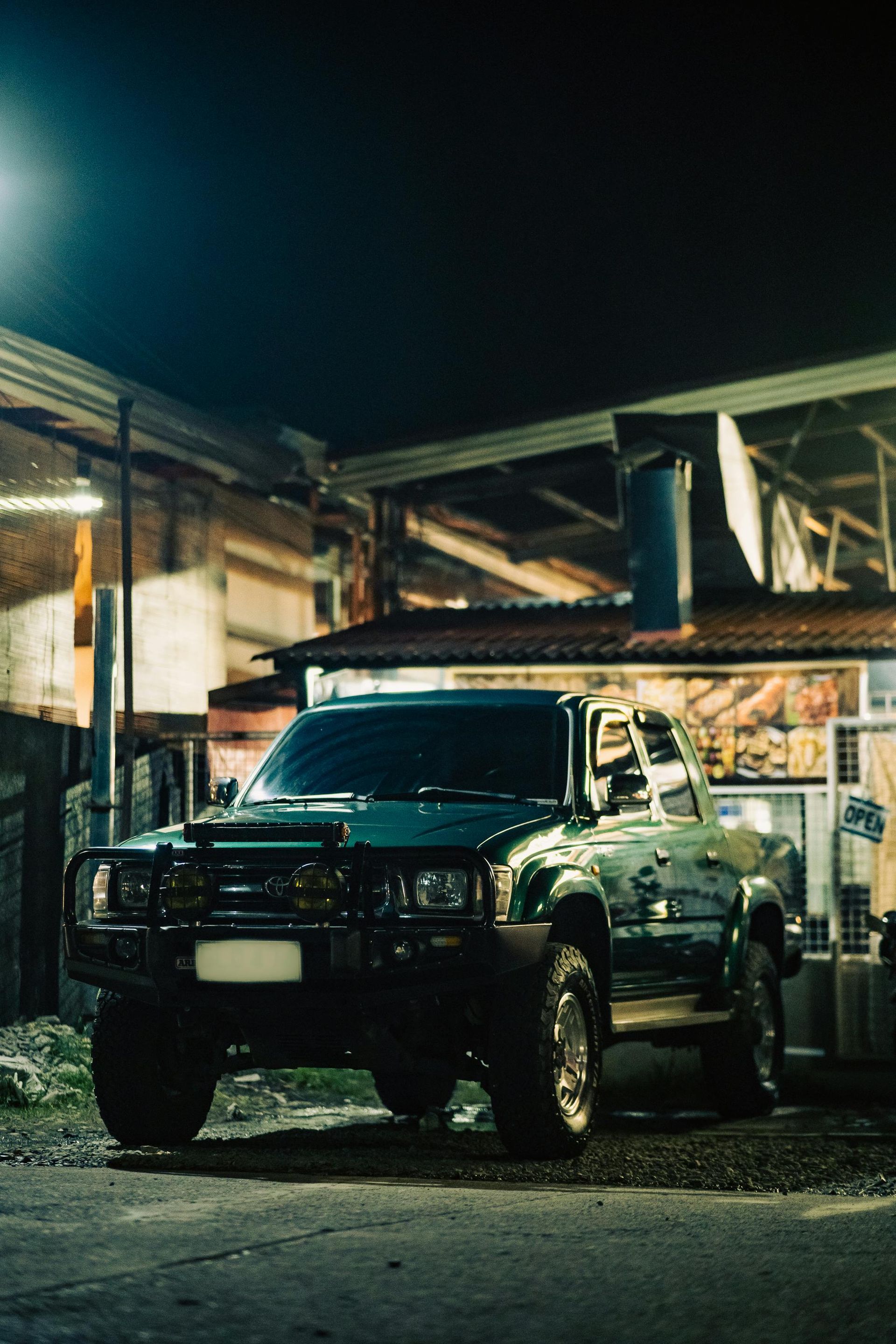 A green truck is parked in front of a building at night.