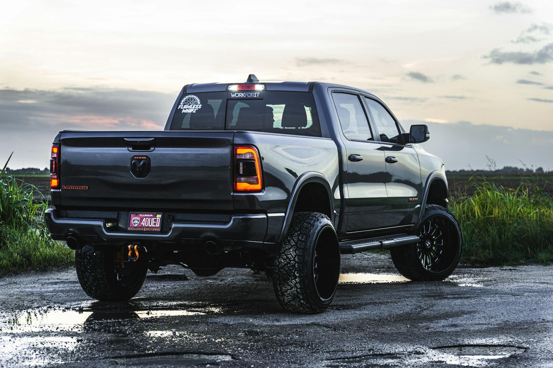 A black truck is parked on a muddy road in a field.