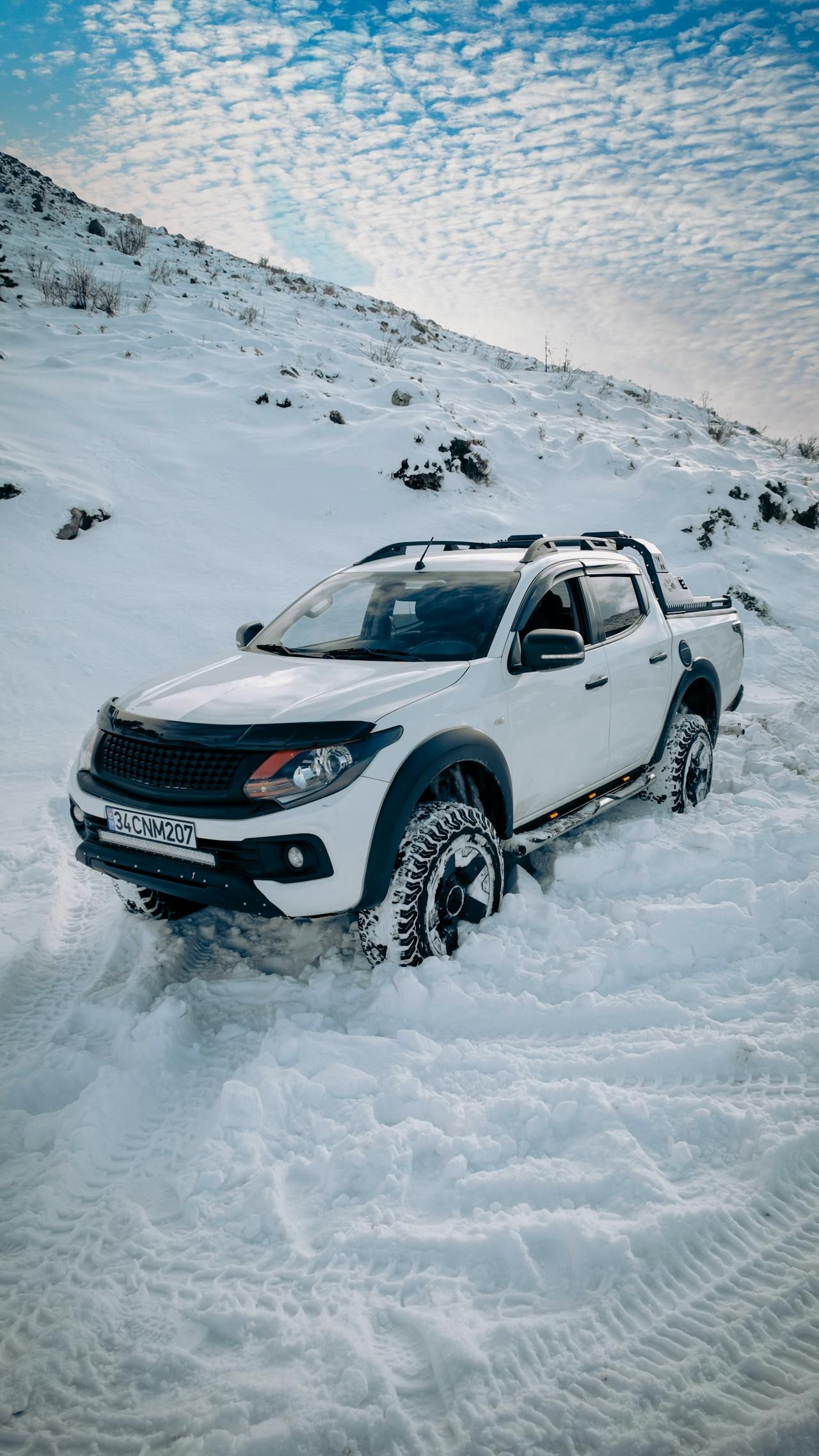 A white truck is driving through the snow on a snowy road.