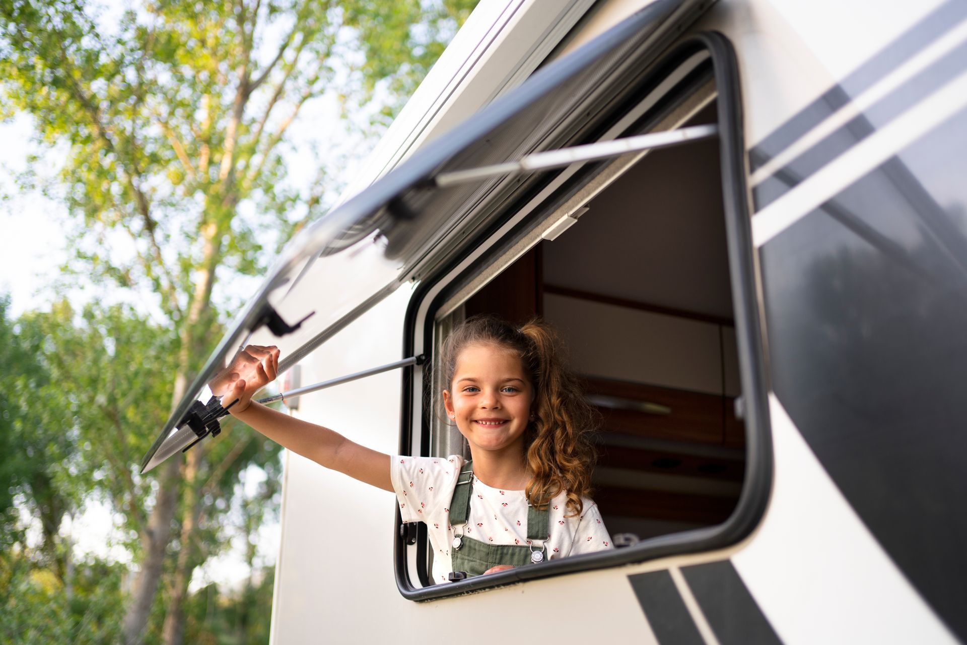 A little girl is looking out of the window of a rv.