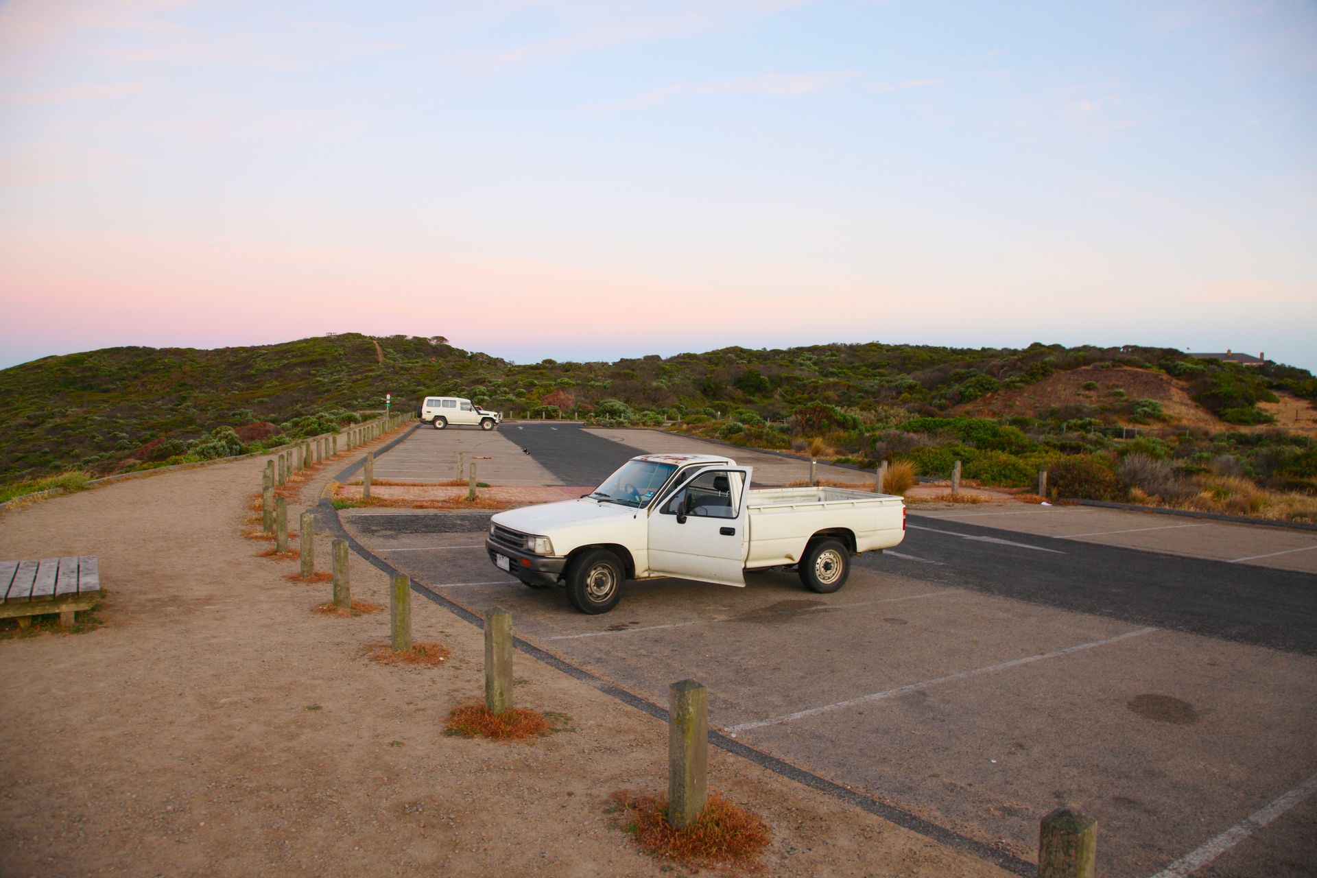 A white truck is parked on the side of the road in a parking lot.