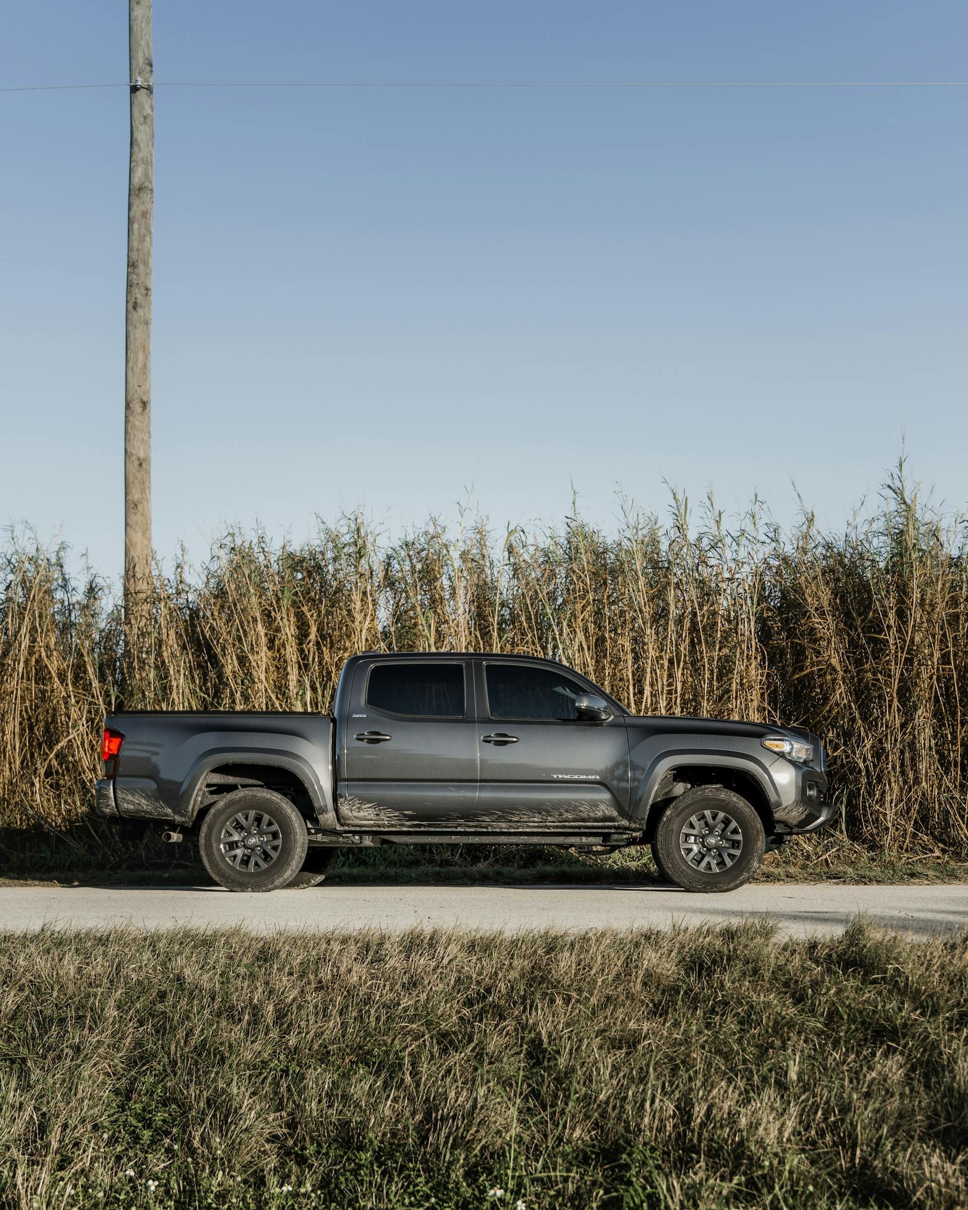 A truck is parked on the side of a dirt road next to a corn field.