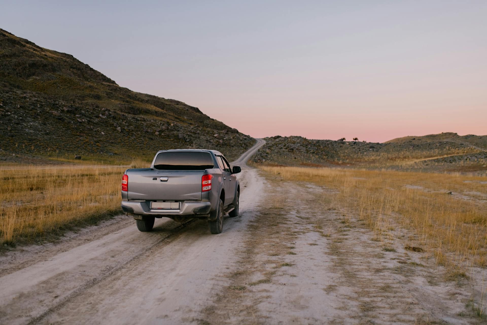 A pickup truck is driving down a dirt road.