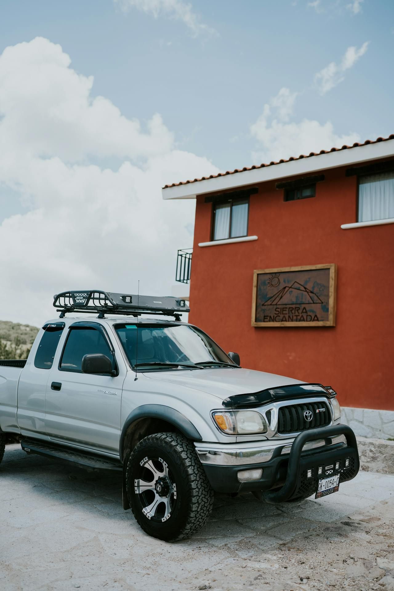 A silver truck with a roof rack is parked in front of a red building.