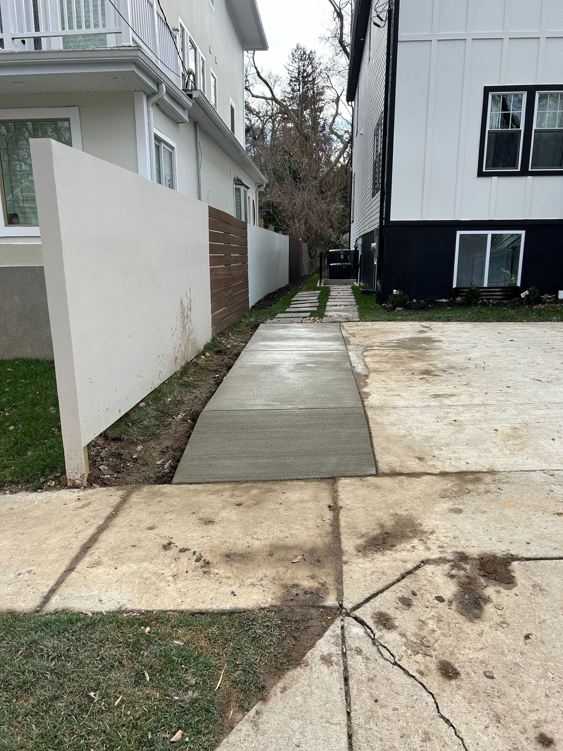 A concrete walkway leading to a house with a lush green lawn.