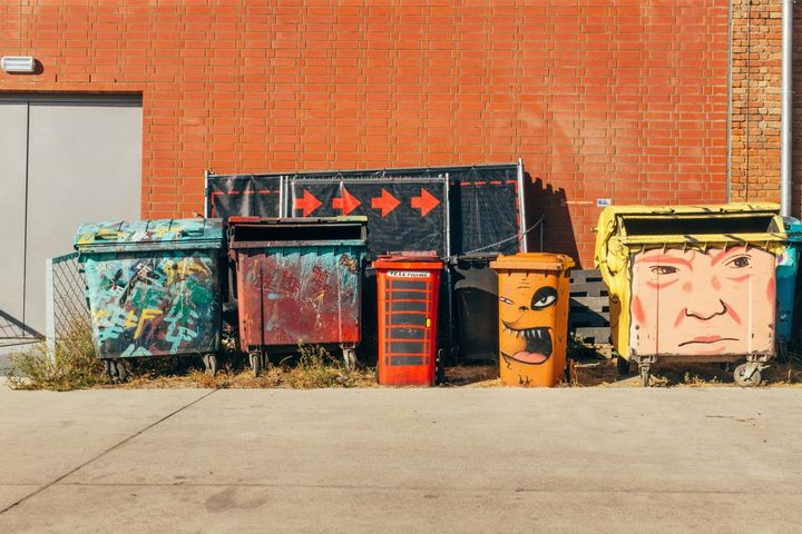 Colorful painted trash bins lined against a red brick wall on a sidewalk