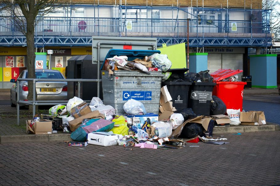 Overflowing trash bins and scattered garbage on a street in front of a building