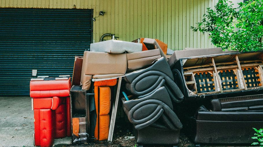 Stack of colorful trash bins and bins piled beside a garage door outdoors