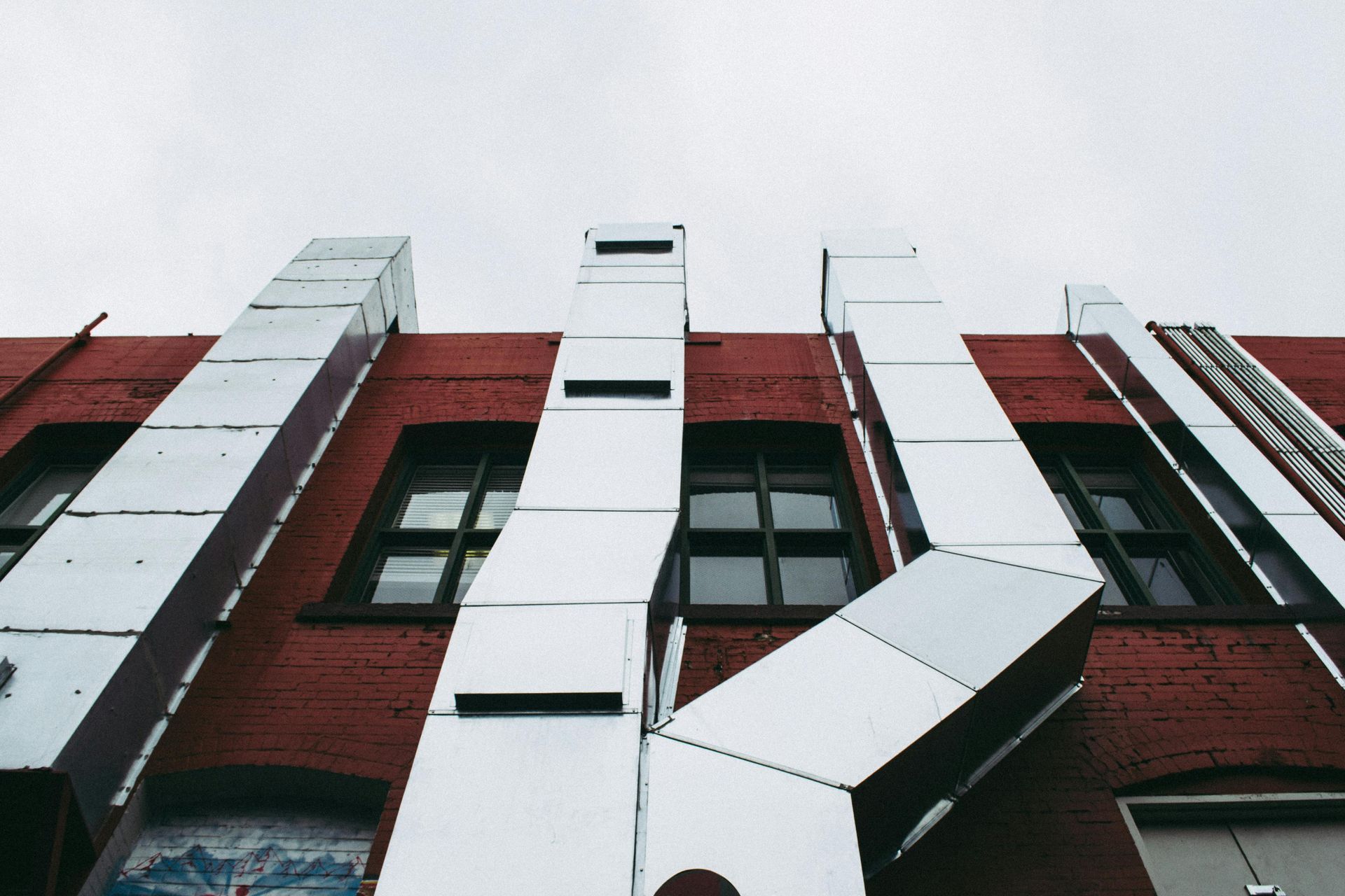 Low-angle view of a red brick building with white vertical panels and windows against a gray sky