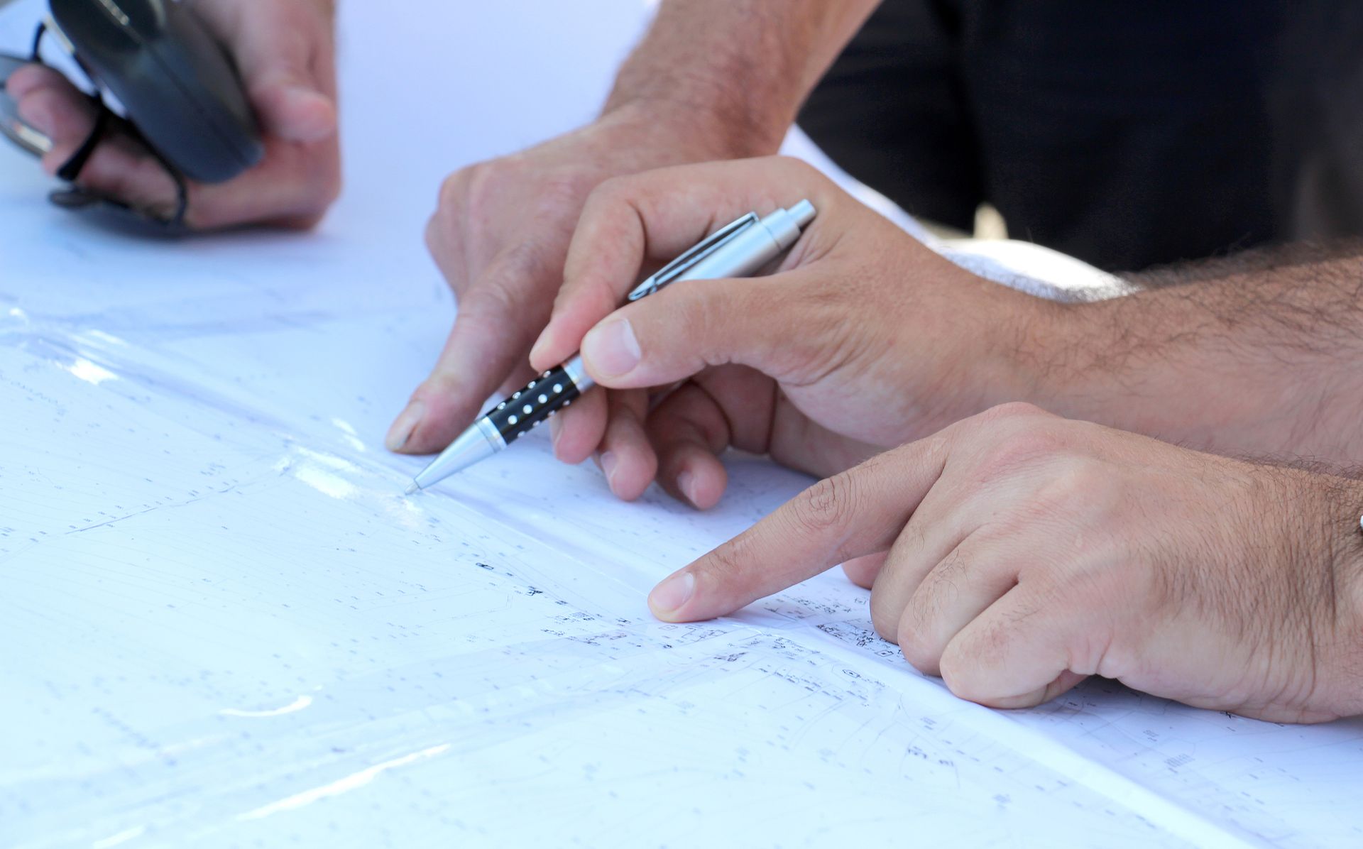Hands pointing and writing on a large white sheet with a pen in a bright workspace.