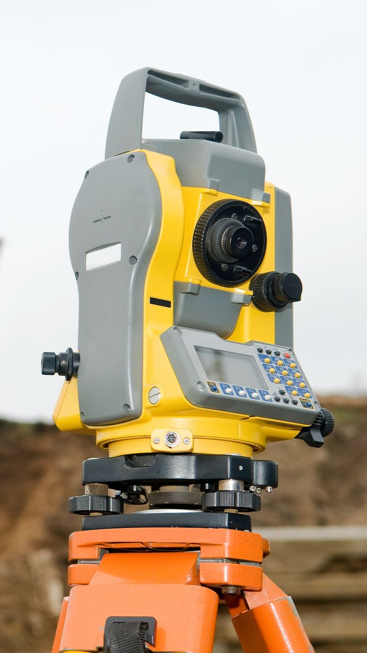 Yellow surveyor’s total station mounted on an orange tripod outdoors