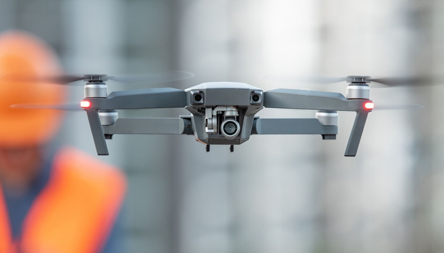 Gray drone flying indoors with blurred orange figure in the background