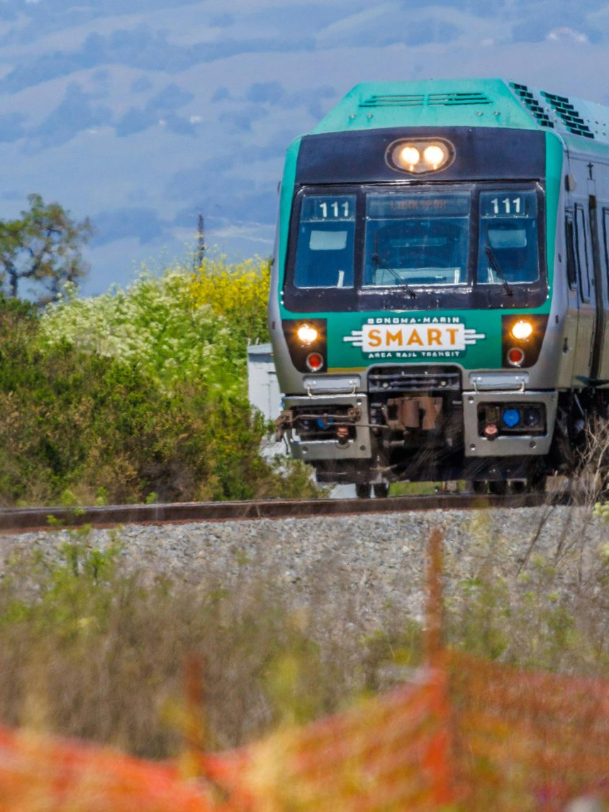 Green and silver train approaching on tracks through a rural landscape