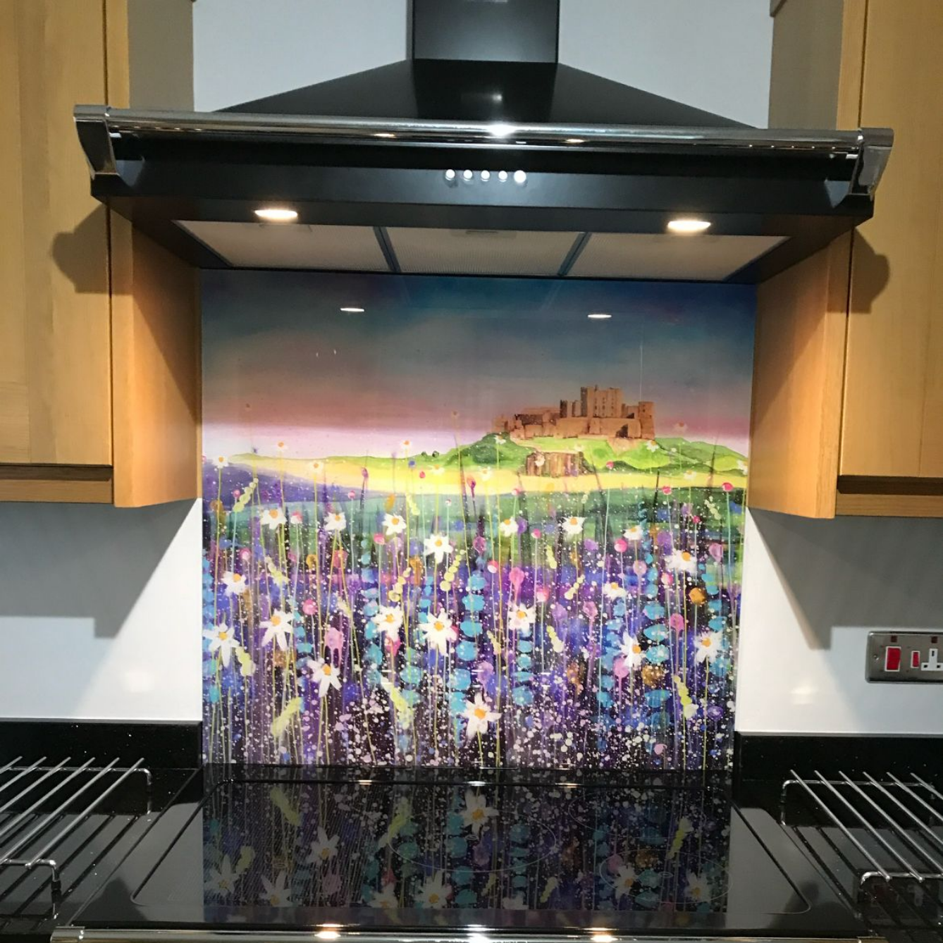 Kitchen stove with black range hood and a colorful landscape backsplash featuring purple flowers and a castle in the distance