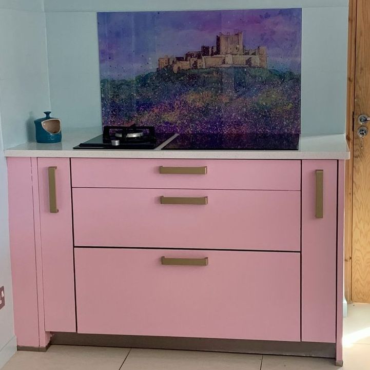 Pink cabinet with drawers and a framed castle painting on top in a light room