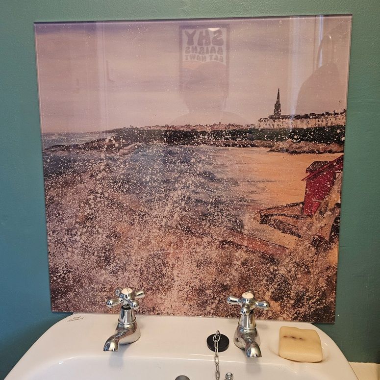 Framed seascape art above a bathroom sink with two silver faucets and a soap bar