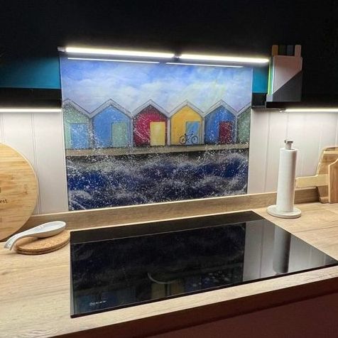 Kitchen counter with glossy black cooktop, colorful house mural, and under-cabinet light above sink area