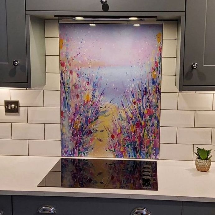 Colorful abstract painting above a kitchen stove, framed by gray cabinets and white subway tile.