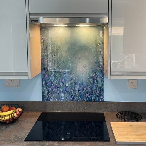 Modern kitchen with black cooktop, stainless range hood, and blue glass backsplash panel