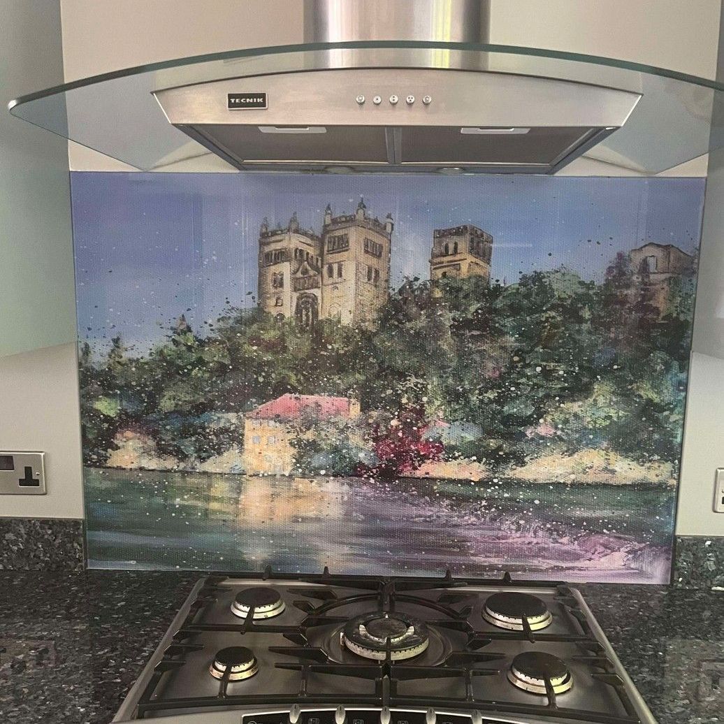 Kitchen backsplash mural of a castle above water with trees and flowers, under a glass range hood