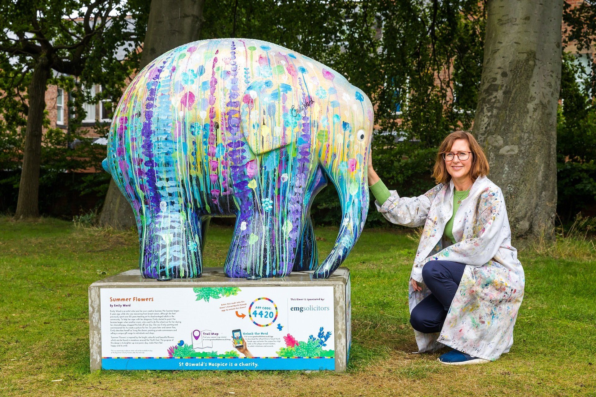 Woman kneeling beside a colorful painted elephant sculpture in a park