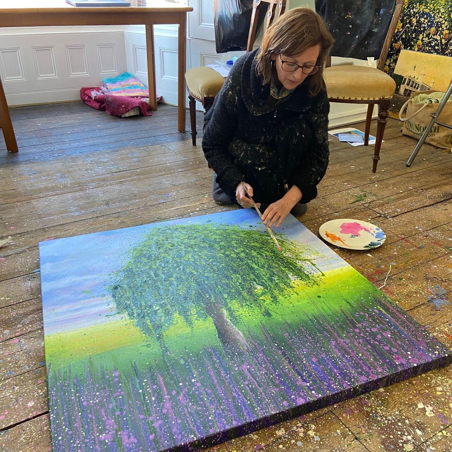 Woman painting a colorful tree mural on a large canvas indoors