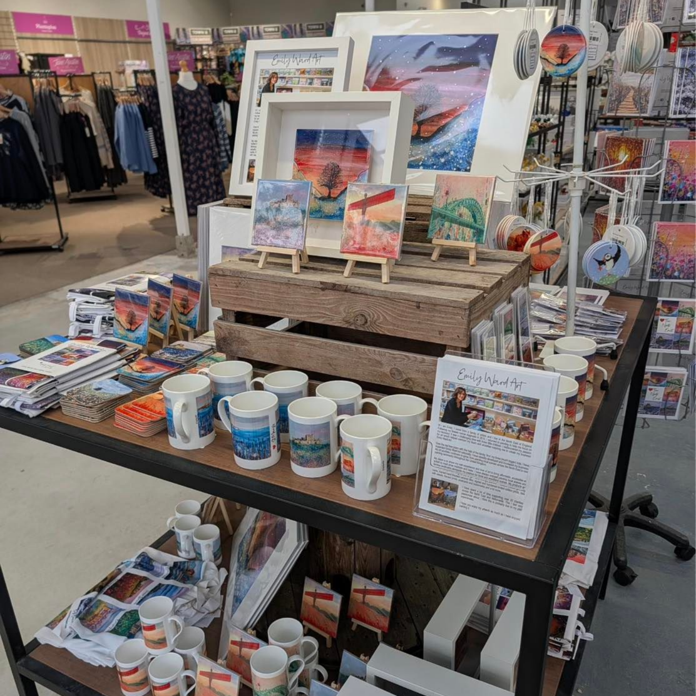 Art vendor display with colorful prints, mugs, and candles on shelves in a store.