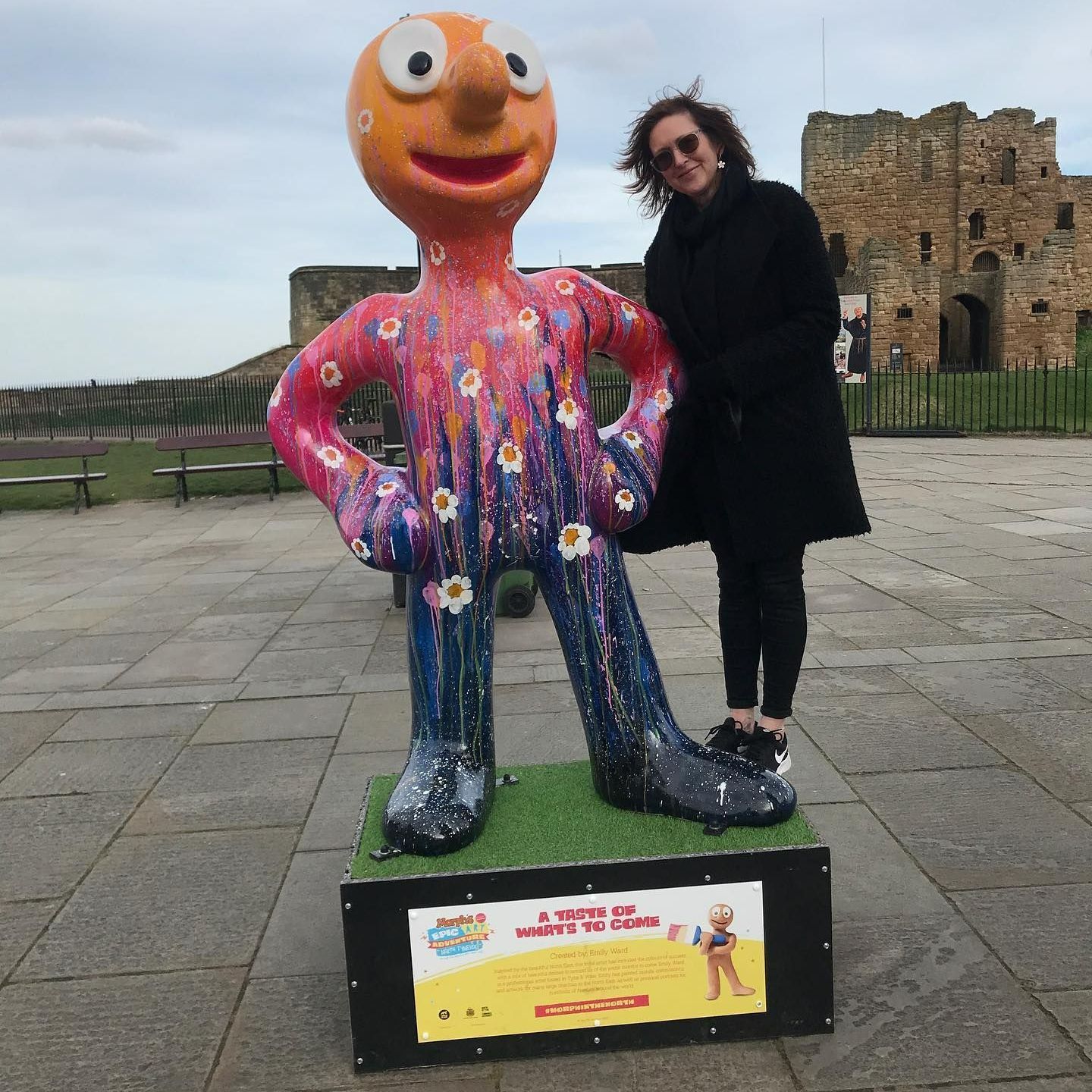Person posing beside a colorful outdoor statue on a stone promenade near ruins.
