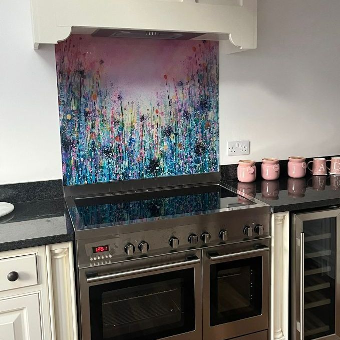 Modern kitchen with stainless stove, colorful abstract backsplash, black countertops, and pink canisters