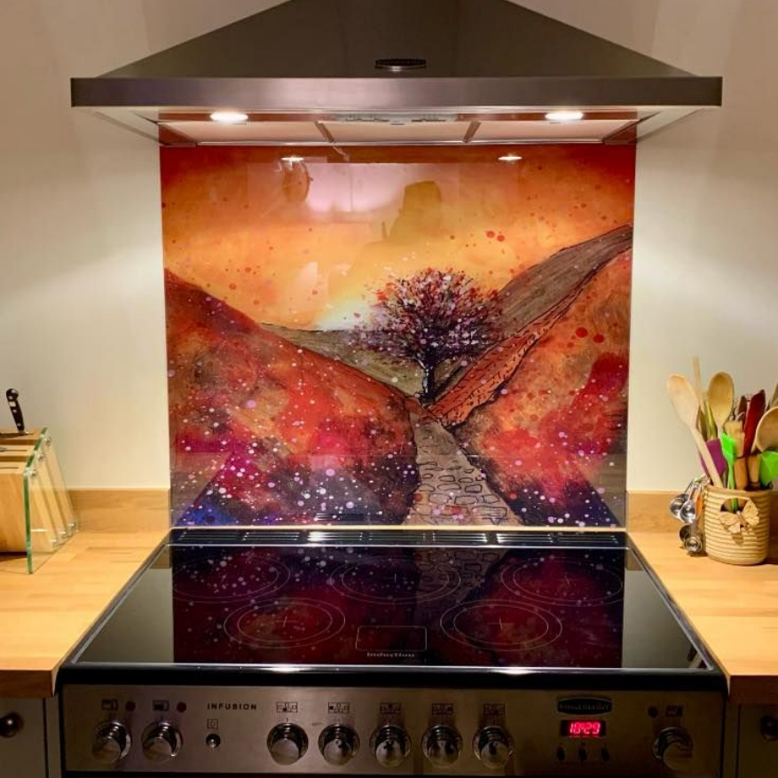 Colorful abstract art backsplash above a stainless steel stove and black glass cooktop in a modern kitchen