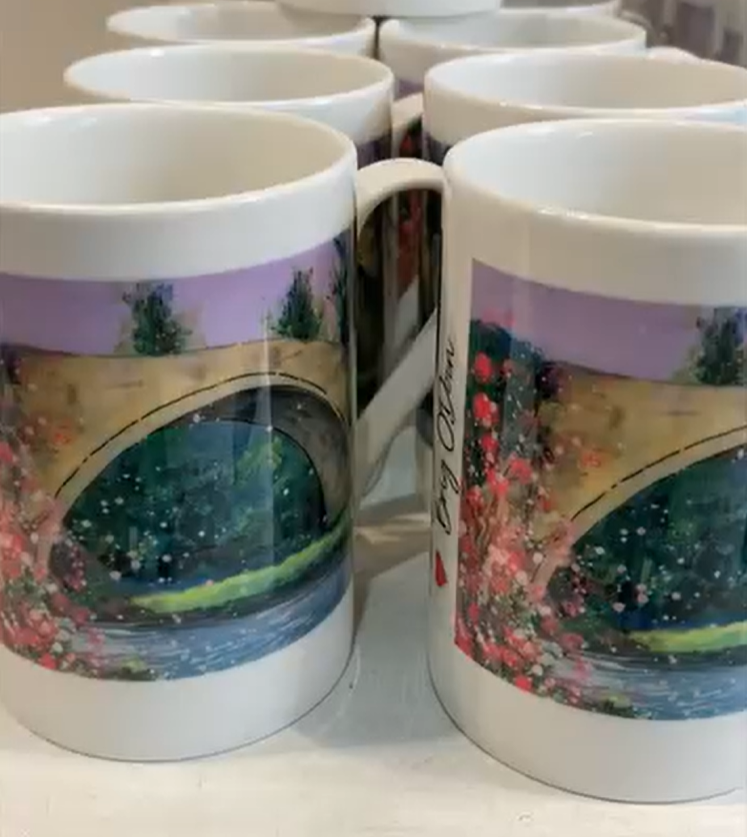 White mugs with a colorful landscape and oval design printed on them, arranged in rows.