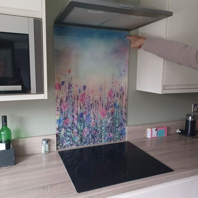 Kitchen with floral backsplash panel under a range hood, hand pointing at it.