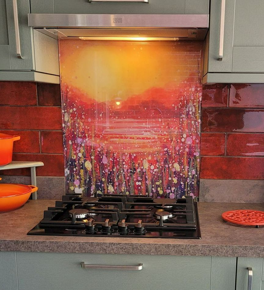 Colorful sunset artwork as a kitchen backsplash above a gas stove, with gray cabinets and red tile walls
