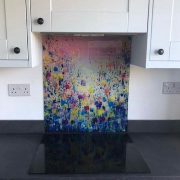 Colorful abstract paint backsplash behind a black stovetop in a white kitchen