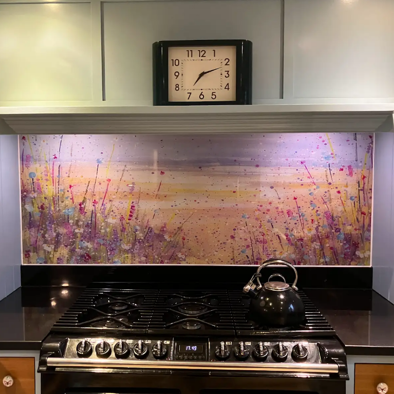 Modern kitchen stove with stainless kettle, black cooktop, pastel backsplash, and wall clock above.
